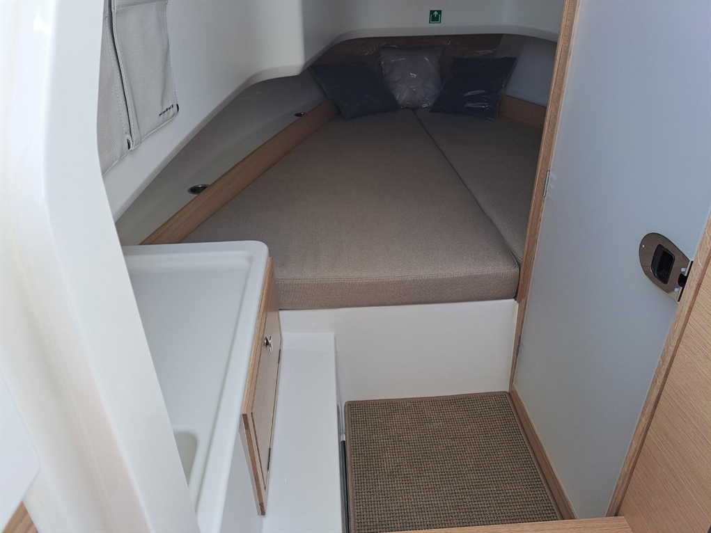Interior of a boat cabin featuring a double berth, drawer storage, and light-colored wood finishes; two pillows on the bed.